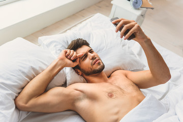 Puzzled guy using mobile phone after sleep