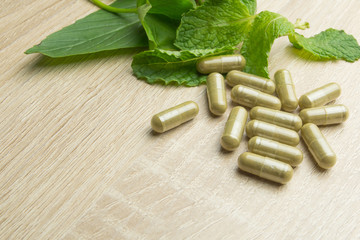 Herbal pills with healthy medical plant. Green leaf, alternative drug on wood ground