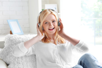 Young woman with headphones listening to music and sitting on the sofa in light room