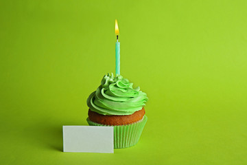 Fresh tasty cupcake with candle and birthday card on green background