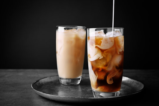 Pouring milk in iced coffee on grey background