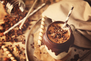 Delicious milkshake with chocolate in a glass jug on a tray, closeup