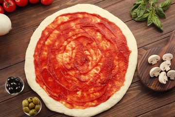 Raw pizza dough with sauce and ingredients on wooden table