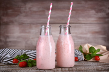 Bottles with delicious strawberry milkshake, napkin and berries on table and wooden background