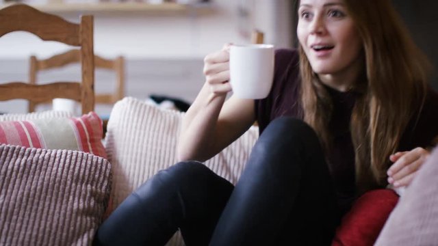 4K Young woman on her couch watching tv reacts in surprise