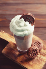 Glass of delicious chocolate milkshake with cookies on wooden board