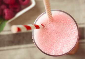 Glass of delicious berry milkshake and fresh raspberry on napkin
