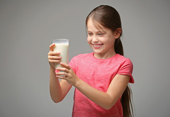 Cute little girl with glass of fresh milk on gray background