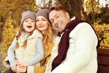 Fototapeta premium Happy family sitting on bench in beautiful autumn park