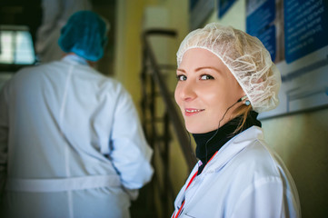 woman in overalls. cute girl smiling, dressed in a white robe and a protective cap, earphone in the ear. Industrial production in the territory of the enterprise