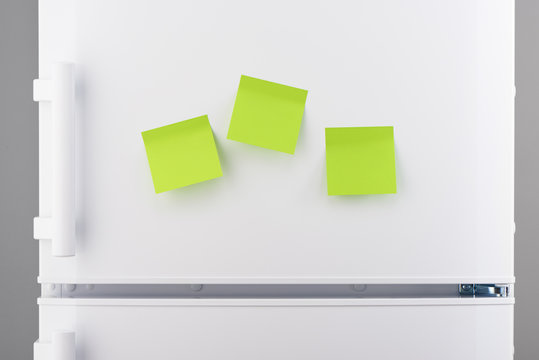 Three blank green sticky paper notes on white refrigerator