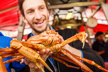 Seller man trader on fish market, keep in hand and show alive big giant crab to customers and smile. Crab kind of crawfish live in ocean and sea and very useful and dietician and delicious food.