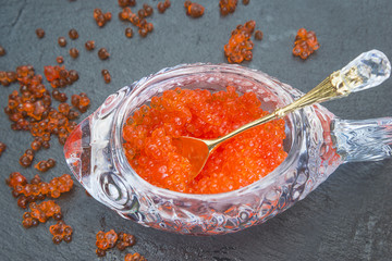 Salmon roe in beautiful caviar bowl with little spoon for caviar on black slate