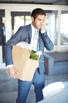 Depressed businessman in office. Shot of a young sad man carrying cardboard box while leaving his workplace.