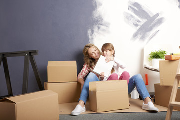 Moving into a new home. Shot of a cute girl helping to unpack the cardboard box to her mother while...