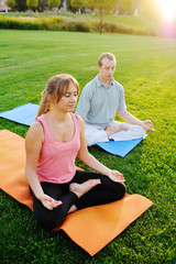 Young man and woman doing yoga on the healing of fresh grass. Healthy lifestyle