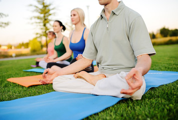 young people in colored clothes doing yoga on fresh grass