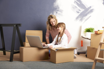 Moving into a new home. Shot of a cute girl helping to unpack the cardboard box to her mother while...