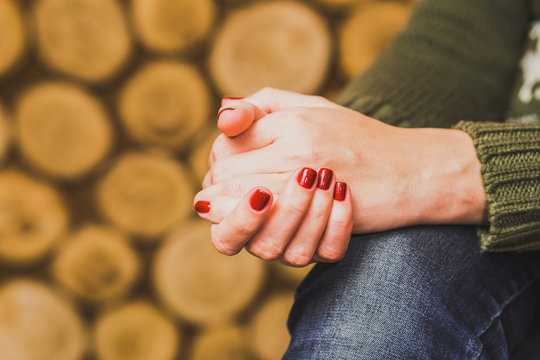 Woman sitting indoors with her hands crossed on knee. Young woman wears green sweater and blue denim jeans. Fingernails with beautiful fresh red manicure. Close up horizontal color photo.