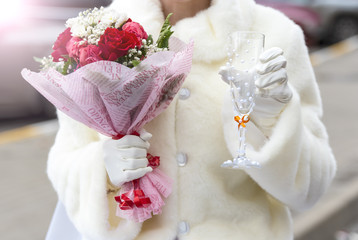 Bouquet of flowers and a glass of champagne in the hands of the bride