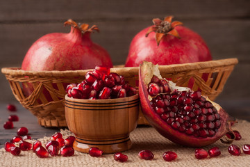 two pomegranate in a wicker basket and grains in the bowl on the old wooden board with sackcloth