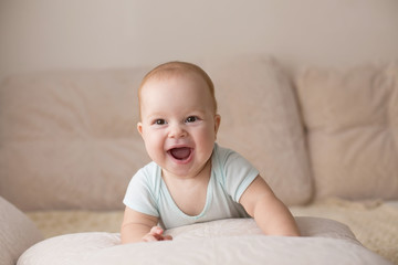 Cute smiling baby in blue bodysuit on a beige couch. - 127852450
