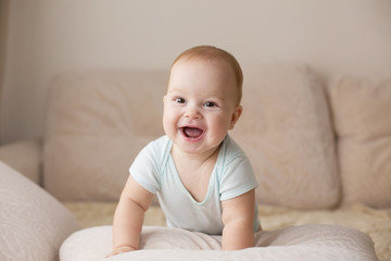 Cute smiling baby in blue bodysuit on a beige couch. - 127852454