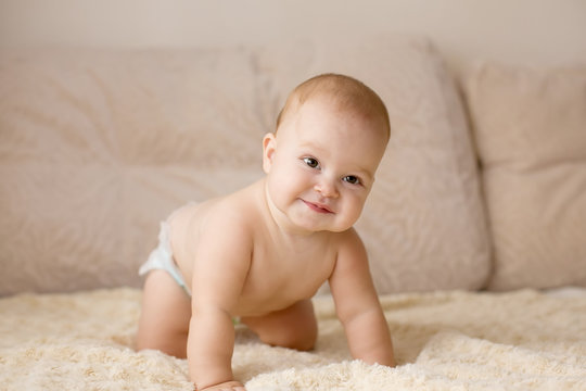 Cute smiling baby in diapers on a beige couch.