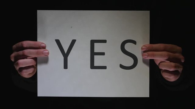 YES sign being showed to the camera by two hands. Black background