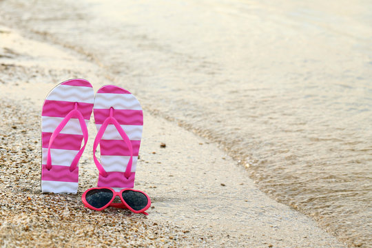 Pink sunglasses with pair of flip flops on the beach sand