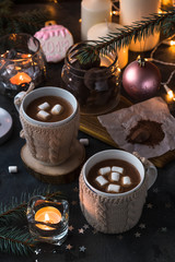 Two cups in knitted mittens of fresh hot cocoa or chocolate on wooden christmas background, dark photo