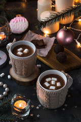 Two cups in knitted mittens of fresh hot cocoa or chocolate on wooden christmas background, dark photo