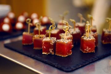 red fish on wooden skewers with the sesame seeds on a black tray