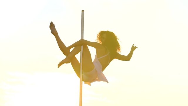 Sexy attractive girl poledancer performs advanced pole dance tricks at sunset on portable dancing stage over the skyline