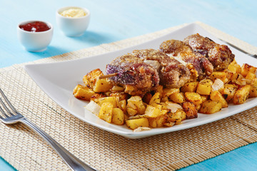 Mince spit on square white dish and roasted potatoes on blue table