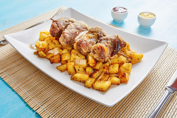 Mince spit on square white dish and roasted potatoes on blue table
