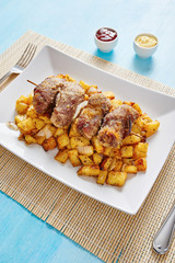 Mince spit on square white dish and roasted potatoes on blue table