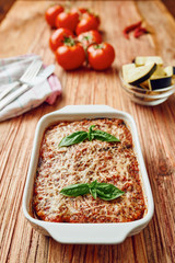 Eggplant parmigiana in white baking sheet tomatoes in backgroud - vegetarian food