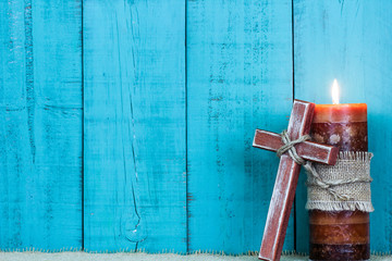 Wooden cross by candle with teal blue wood background