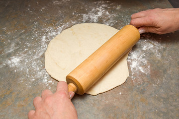 Rolling dough with a wooden roller on the table in the kitchen for meat pies or pizza, or cakes for Christmas time. Homemade pastries. Healthy eating lifestyle.