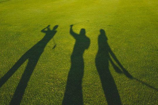 Three golfers with open hands silhouette on grass