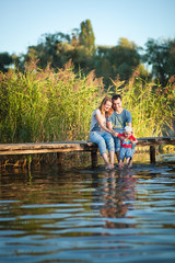 Family, mother, father and child playing and spending time with his young son in the summer the river or lake