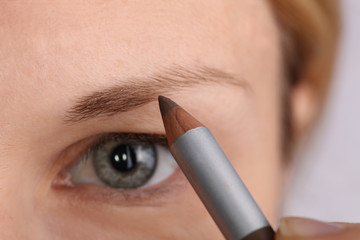Young beautiful woman applying eyebrow pencil close up. Beauty, make up concept