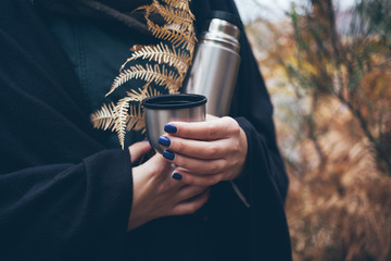 Woman traveler hands holding thermos bottle and cup of tea, walking in autumn forest. Adventure, travel, tourism and camping concept. - obrazy, fototapety, plakaty