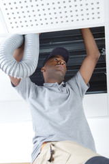 young african male electrician on stepladder fitting ventilation