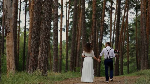 Young couple of hipsters stretches into the distance in the coniferous forest. The camera movement.
