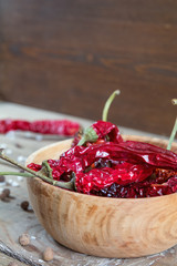 Dried chili peppers in a wooden bowl, salt and pepper on dark wooden table