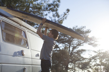 An adult man putting a surfboard on top of a van.  Torrey Pines State Park, San Diego, California.