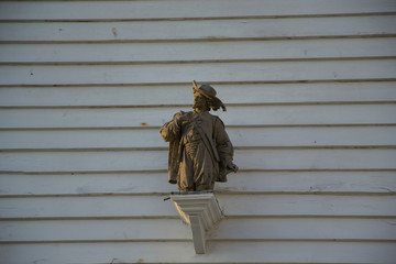 Little statue on a white wall. On the side of building, a statue is decorating the center of an English village.
