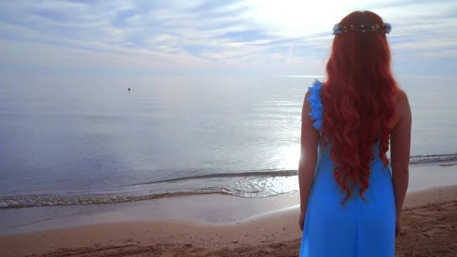 Redhead woman looking at sea. Rear view woman beach. Woman on sea beach. Woman relaxing on sea coast. Girl standing near ocean. Woman beach sunset. Loneliness concept. Dreaming woman. Woman sea sunset
